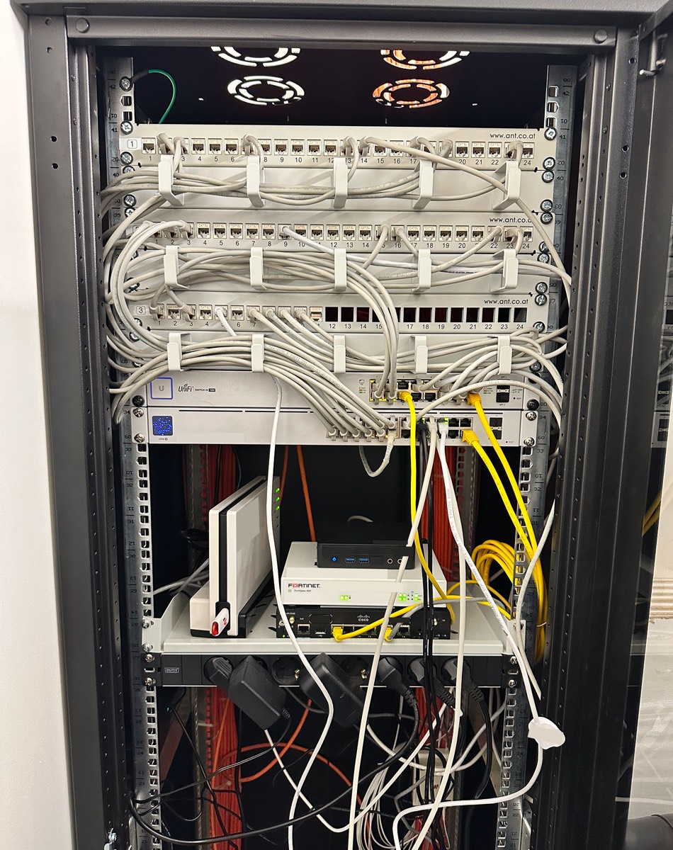 Vorher: gewachsener Schrank an einem der drei Standorte. FortiGate im Lizenzvertrag, lose Netzteile, Kabel kreuz und quer, nichts dokumentiert.