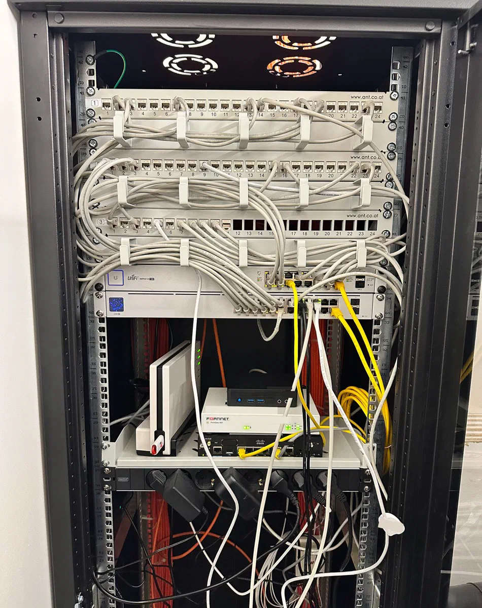 Netzwerkschrank vor der Neuplanung: ungeordnete Kabel, lose Netzteile und verschachtelte Geräte